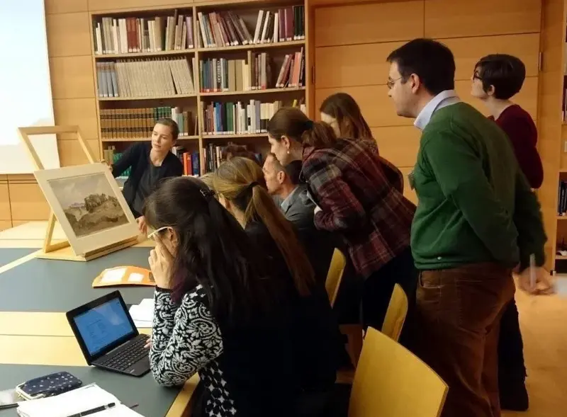 mehrere Personen betrachten Kupferstiche in einem Lesesaal