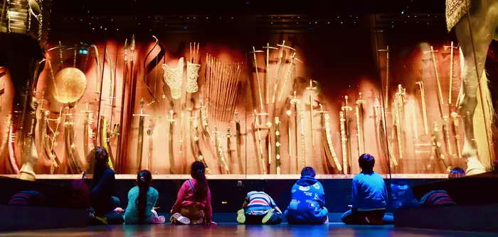 Kinder sitzen vor einer langen Vitrine mit Waffen in der Türckischen Kammer