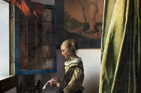 Eine Frau steht vor einem Fester und liest einen Brief