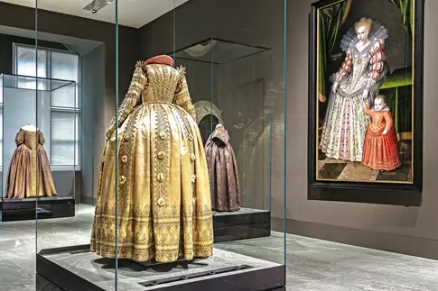 Raum mit prächtigen Kleidern in Vitrinen und einem Gemälde an der Wand