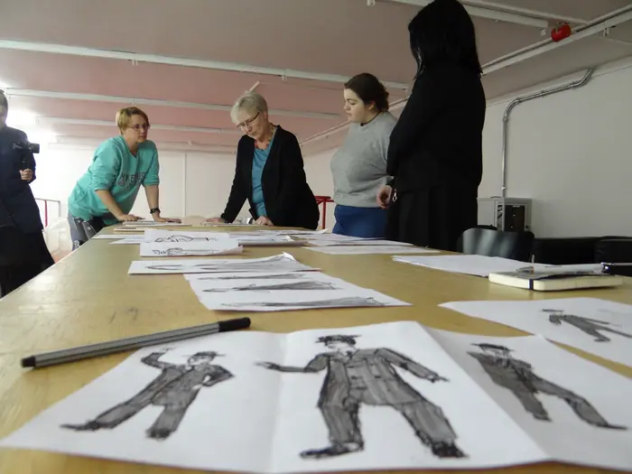 Jugendliche und Erwachsene betrachten viele Zeichnungen an einem großen Tisch