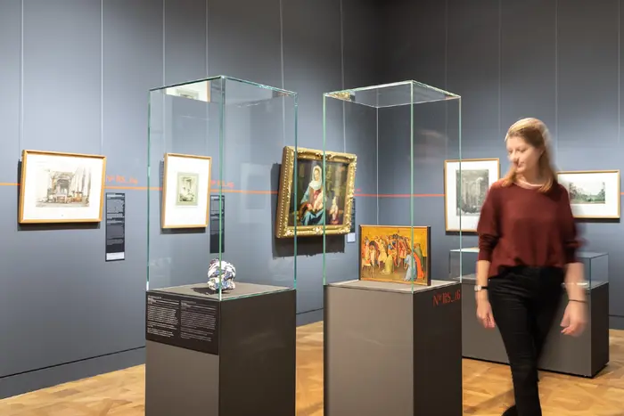 Ausstellungsraum mit Vitrinen, Gemälden und einer Besucherin