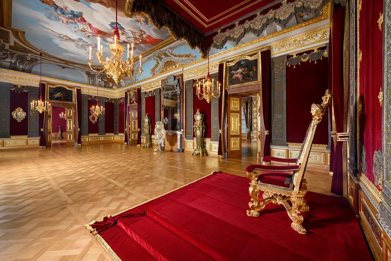 Thron in großem, prunkvollen Raum mit Deckenmalerei und Goldelementen