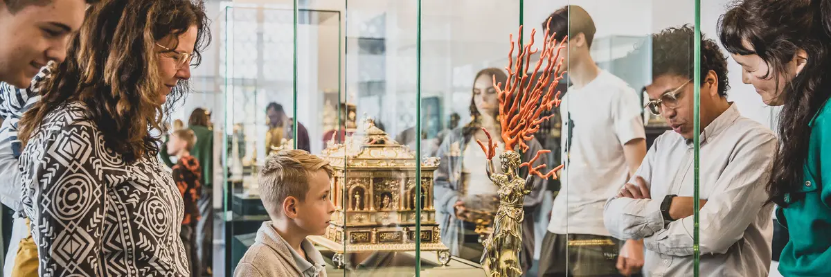 Besucher, die sich eine goldene Figur mit Korallen in einer Vitrine anschauen