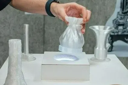 Eine Hand, die nach Vasen-ähnlichen Objekten auf einem weißen Tisch greift